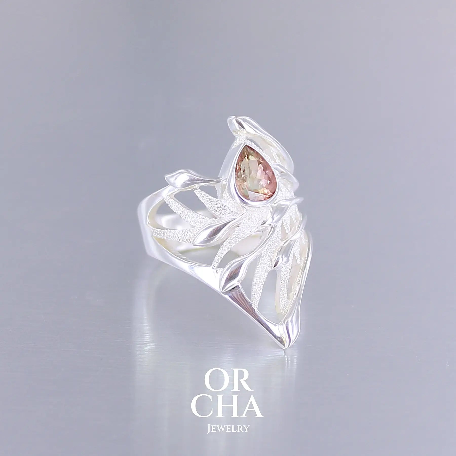 Profil d'une grande Bague pour femme, feuillage tropicale travaillé en filigrane en argent massif, sertie d'une Tourmaline bicolore rose pêche et verte kaki. Pierre facettée en forme de goutte. Pierre incolore, très lumineuse et propre à l'oeil. Taille 56. Bijoux unique, éthique et durable présenté dans un coffret de notre marque, prêt à offrir. Livraison offerte, certificat d'authenticité, service client.