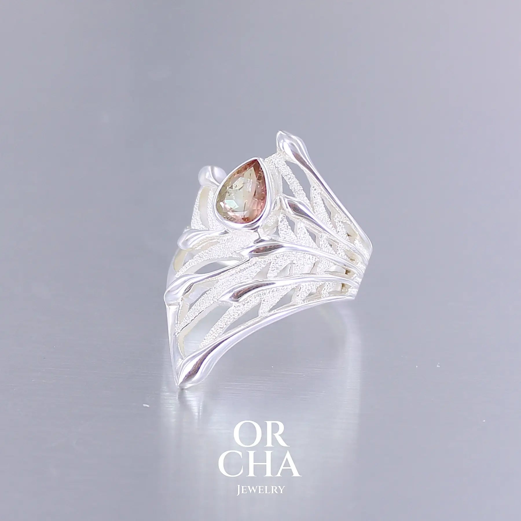 Profil d'une grande Bague pour femme, feuillage tropicale travaillé en filigrane en argent massif, sertie d'une Tourmaline bicolore rose pêche et verte kaki. Pierre facettée en forme de goutte. Pierre incolore, très lumineuse et propre à l'oeil. Taille 56. Bijoux unique, éthique et durable présenté dans un coffret de notre marque, prêt à offrir. Livraison offerte, certificat d'authenticité, service client.