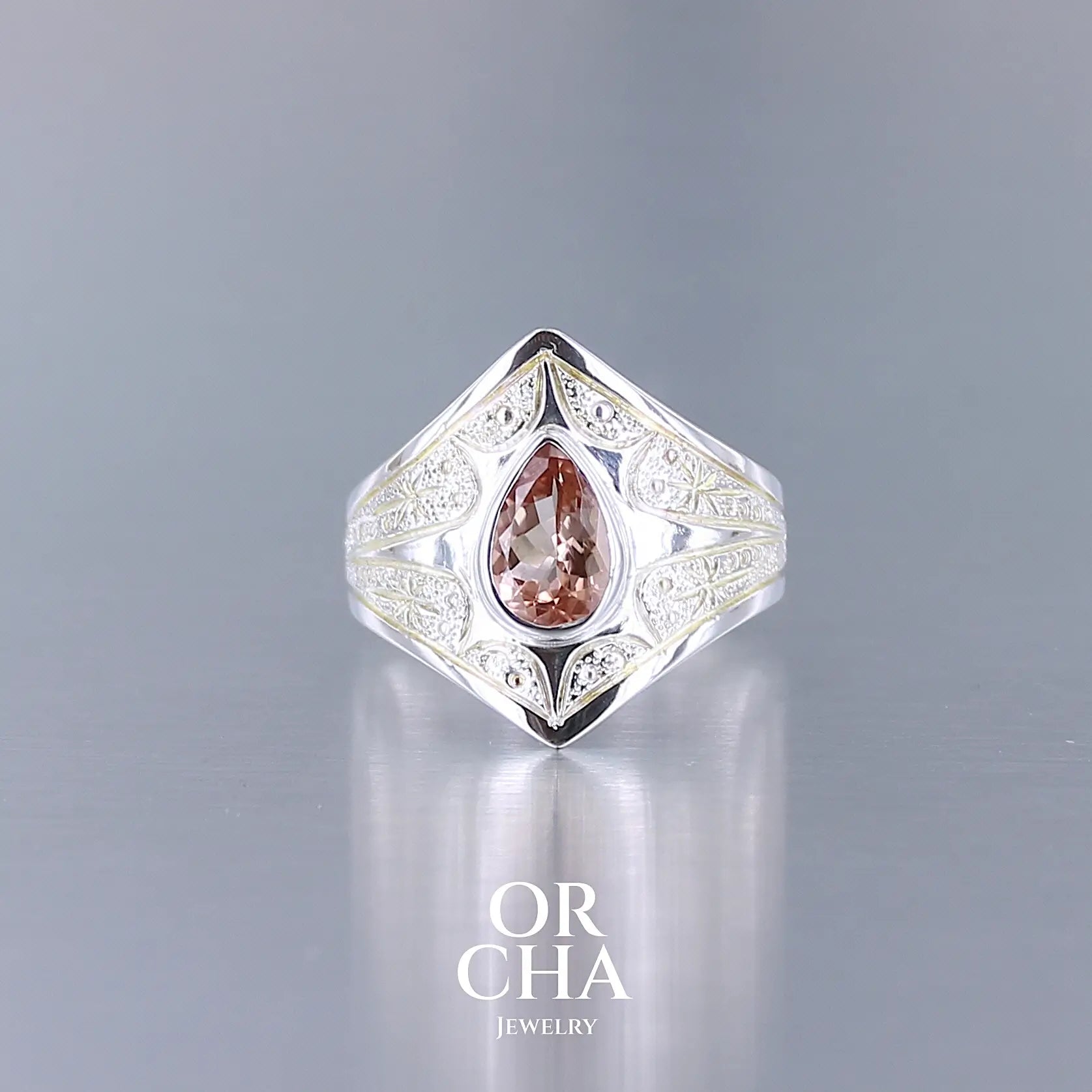 Bague pour femme en argent massif sculptées d'étoiles et autres corps célestes sertie d'une Tourmaline rose ambré. Pierre facettée en forme de goutte, pierre naturelle de qualité transparente propre à l'oeil. Taille 59. Bijoux unique, éthique et durable présenté dans un coffret de notre marque, prêt à offrir. Livraison offerte, certificat d'authenticité, service client.