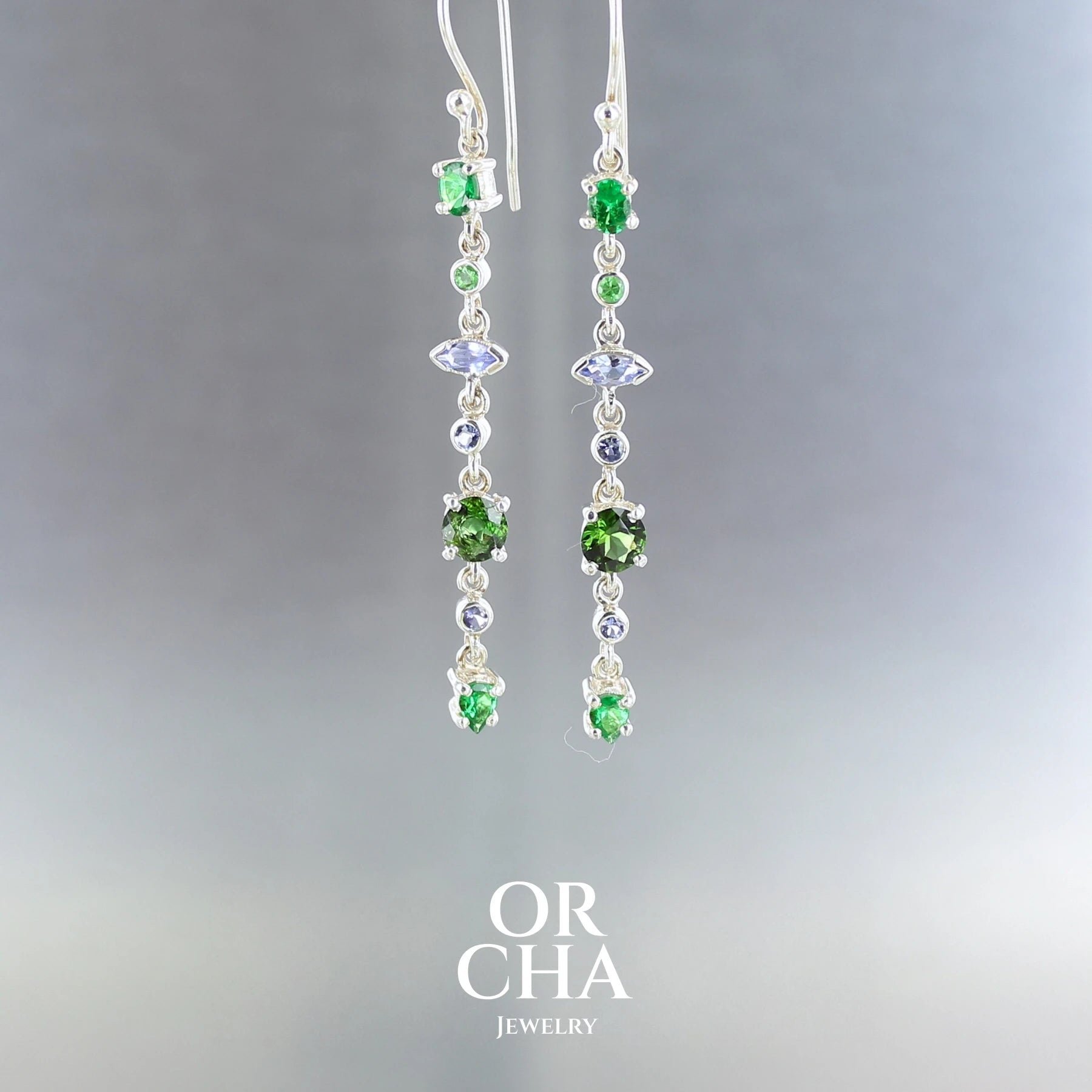 Boucles d'oreilles pendantes, pour femme, réalisées en argent sterling 925, ornées de Tourmalines vertes de Grenats tsavorites et de Tanzanites, un total de 14 pierres semi précieuses naturelles. Monture de qualité à la fois solide et délicate, travaillée de manière traditionnelle