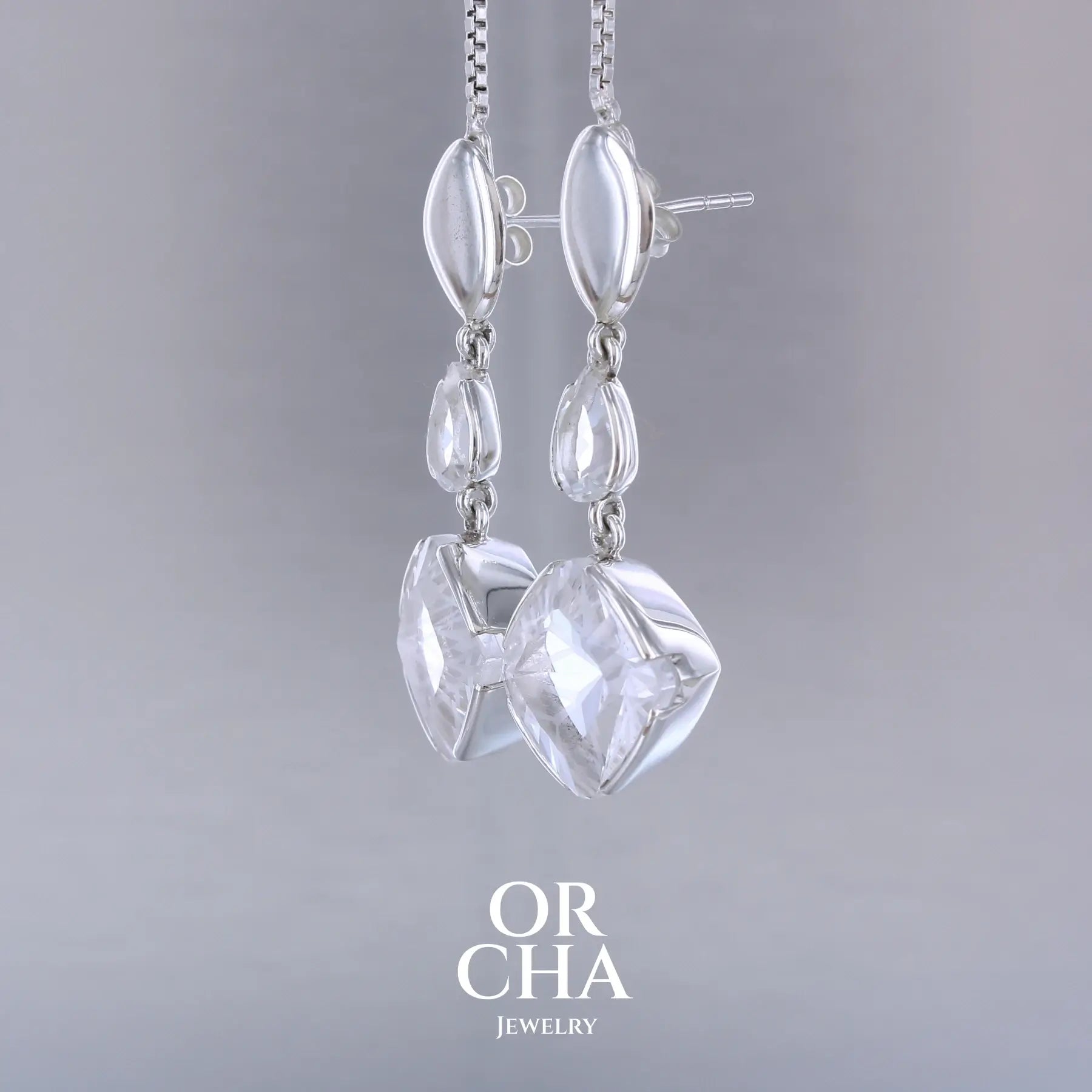 Boucles d'oreilles pendantes pour femme en argent massif serties de Cristals de roche gravés d'étoiles et de topazes blanches. Pierres facettée de forme carrée et goutte de qualité transparente, propre à l'oeil. Pierre naturelle incolore et blanche sur les parties gravées. Boucles de 3,7 cm de long. Bijoux unique, éthique et durable présenté dans un coffret de notre marque, prêt à offrir. Livraison offerte, certificat d'authenticité, service client.
