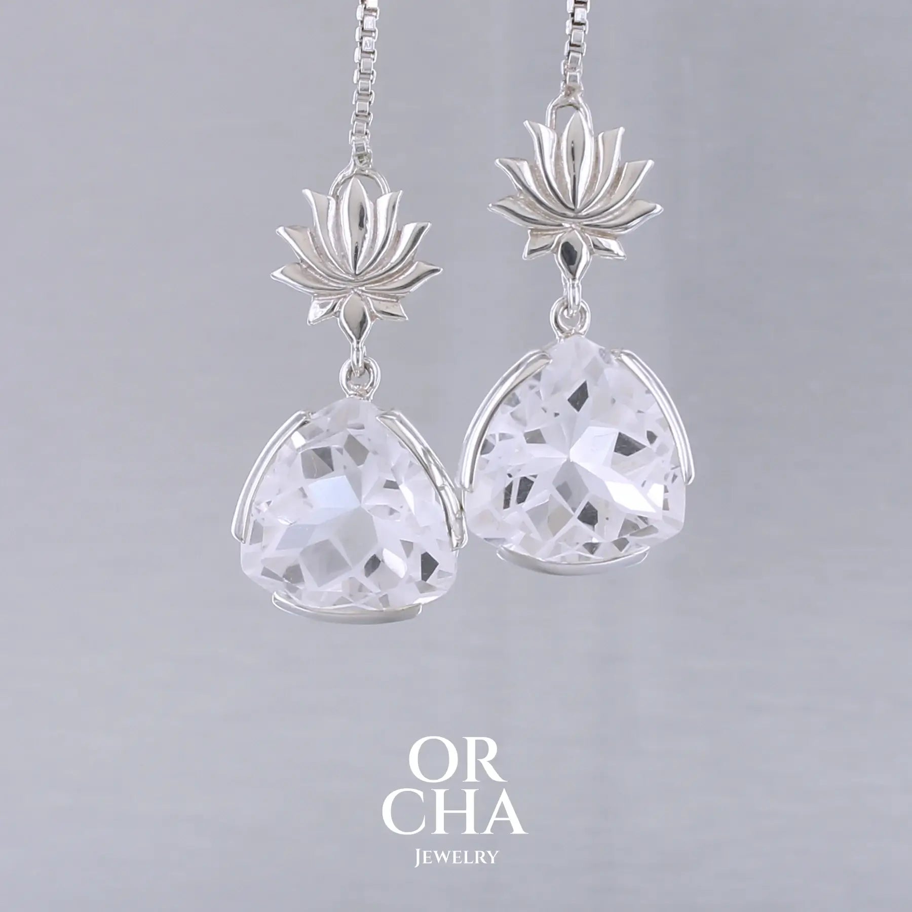 Boucles d'oreilles pour femme en argent massif sertie de Cristals de roche gravés de fleurs de vie. Pierres facettées de forme triangulaire de qualités transparentes, propre à l'oeil. Pierre naturelle incolore et blanche sur les parties gravées. Le clou des boucles représente un lotus. Bijoux unique, éthique et durable présenté dans un coffret de notre marque, prêt à offrir. Livraison offerte, certificat d'authenticité, service client.