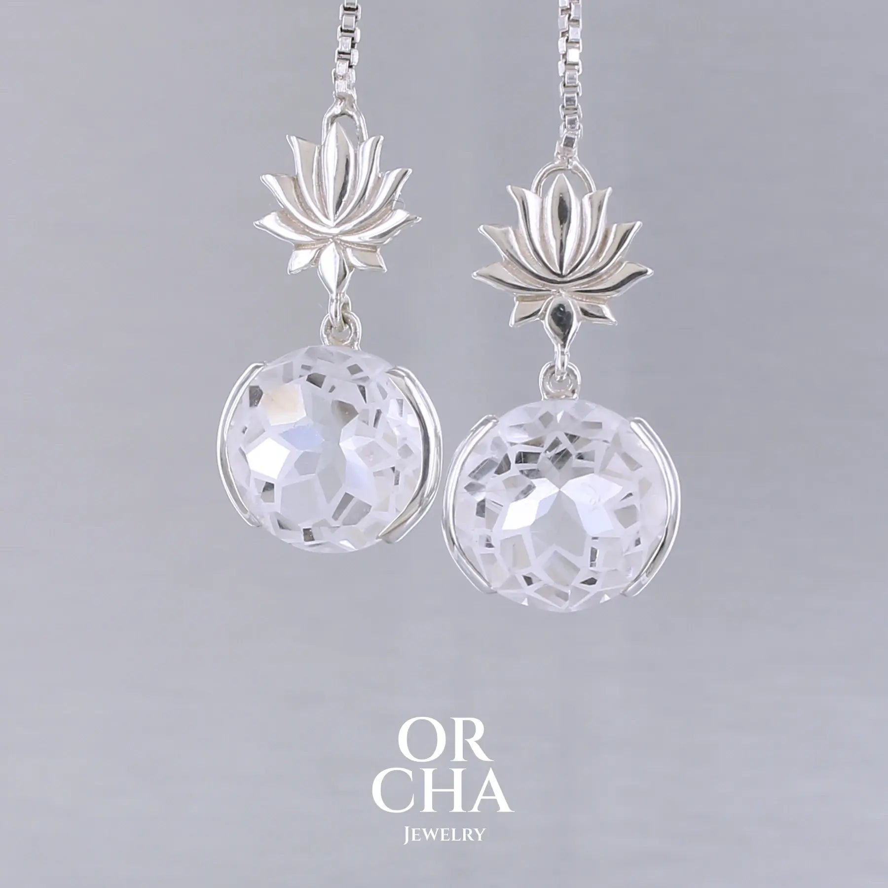 Boucles d'oreilles pour femme en argent massif sertie de Cristals de roche gravés de fleurs de vie. Pierres facettées de forme ronde de qualités transparentes, propre à l'oeil. Pierre naturelle incolore et blanche sur les parties gravées. Le clou des boucles représente un lotus. Bijoux unique, éthique et durable présenté dans un coffret de notre marque, prêt à offrir. Livraison offerte, certificat d'authenticité, service client.
