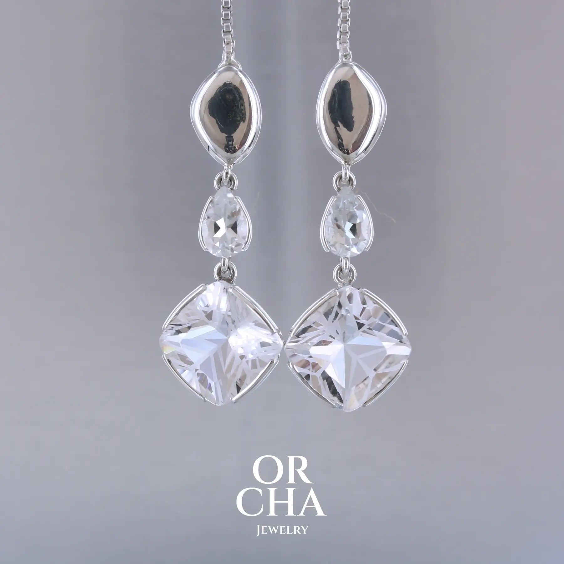 Boucles d'oreilles pendantes pour femme en argent massif serties de Cristals de roche gravés d'étoiles et de topazes blanches. Pierres facettée de forme carrée et goutte de qualité transparente, propre à l'oeil. Pierre naturelle incolore et blanche sur les parties gravées. Boucles de 3,7 cm de long. Bijoux unique, éthique et durable présenté dans un coffret de notre marque, prêt à offrir. Livraison offerte, certificat d'authenticité, service client.