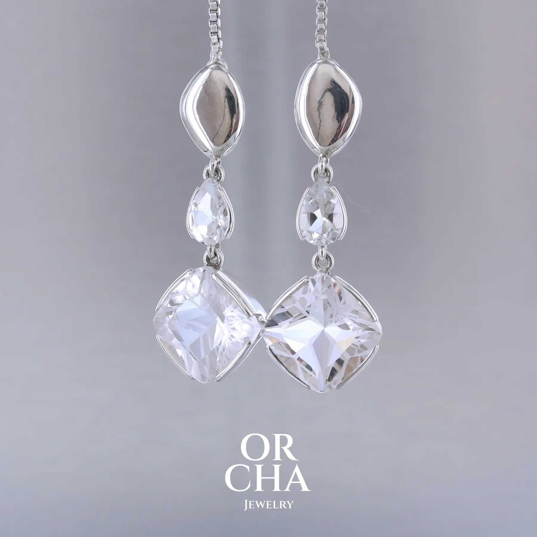 Boucles d'oreilles pendantes pour femme en argent massif serties de Cristals de roche gravés d'étoiles et de topazes blanches. Pierres facettée de forme carrée et goutte de qualité transparente, propre à l'oeil. Pierre naturelle incolore et blanche sur les parties gravées. Boucles de 3,7 cm de long. Bijoux unique, éthique et durable présenté dans un coffret de notre marque, prêt à offrir. Livraison offerte, certificat d'authenticité, service client.
