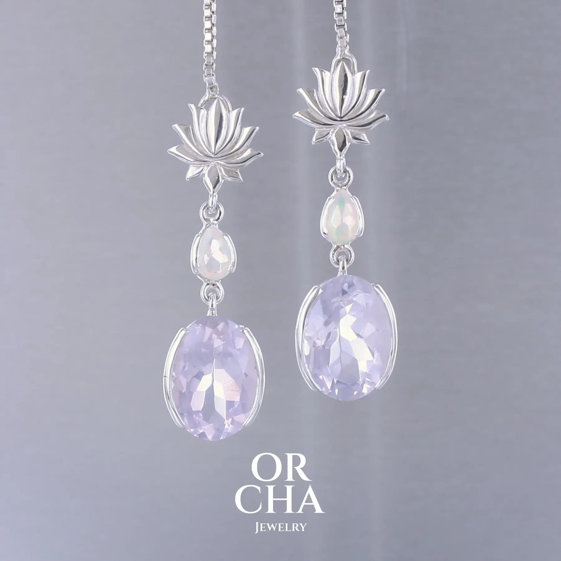Boucles d'oreilles Lotus pour femme en argent massif sertie de Quartz lavandes et d'opales d'Éthiopie. Pierres facettées de forme ovales et de gouttes de qualités transparentes, propre à l'oeil. Pierres naturelles de couleurs violettes pastel teintées de rose avec des reflets opalescents et multicolores pour les opales . Bijoux unique, éthique et durable présenté dans un coffret de notre marque, prêt à offrir. Livraison offerte, certificat d'authenticité, service client.