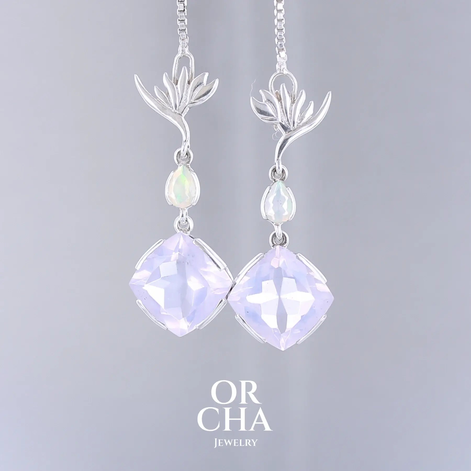 Boucles d'oreilles Strelitzia pour femme en argent massif sertie de Quartz lavandes et d'opales d'Éthiopie. Pierres facettées de forme ovales et de gouttes de qualités transparentes, propre à l'oeil. Pierres naturelles de couleurs violettes pastel teintées de rose avec des reflets opalescents et multicolores pour les opales . Bijoux unique, éthique et durable présenté dans un coffret de notre marque, prêt à offrir. Livraison offerte, certificat d'authenticité, service client.