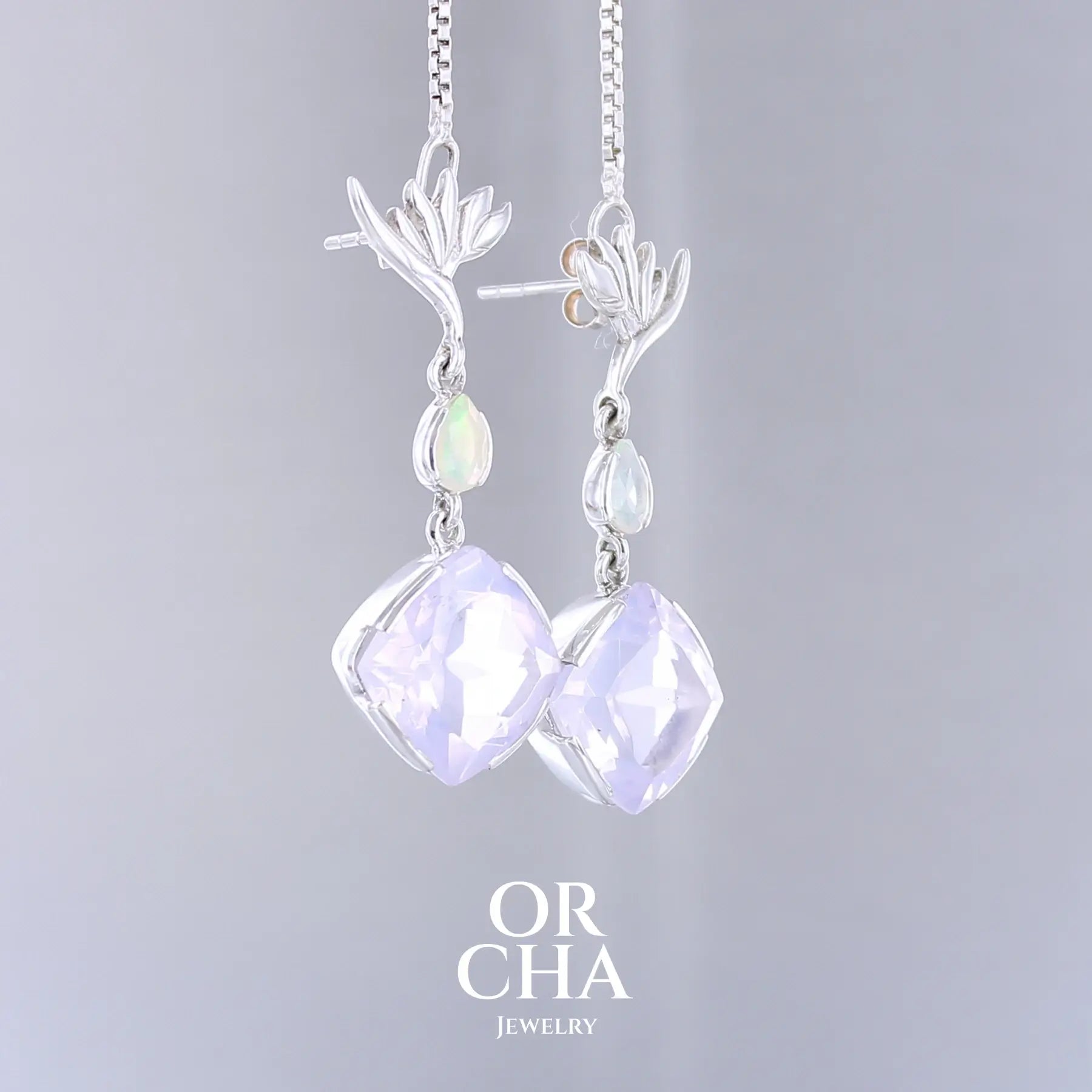 Boucles d'oreilles Strelitzia pour femme en argent massif sertie de Quartz lavandes et d'opales d'Éthiopie. Pierres facettées de forme ovales et de gouttes de qualités transparentes, propre à l'oeil. Pierres naturelles de couleurs violettes pastel teintées de rose avec des reflets opalescents et multicolores pour les opales . Bijoux unique, éthique et durable présenté dans un coffret de notre marque, prêt à offrir. Livraison offerte, certificat d'authenticité, service client.