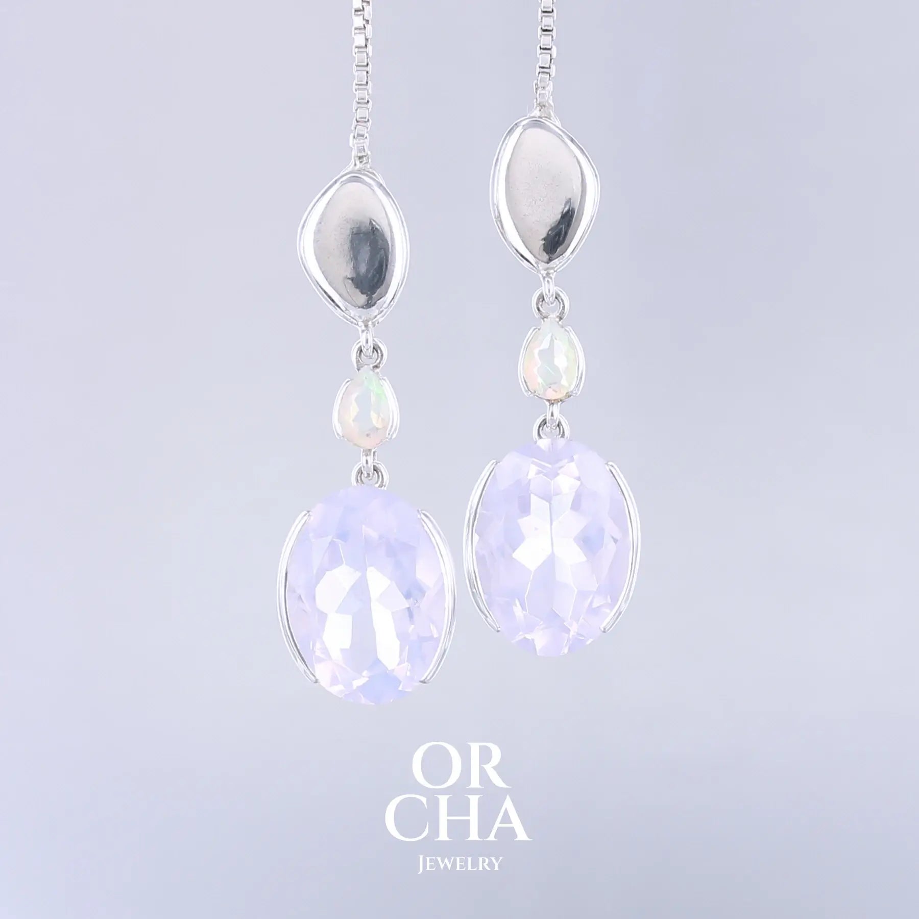 Boucles d'oreilles pour femme en argent massif sertie de Quartz lavandes et d'opales d'Éthiopie. Pierres facettées de forme ovales et de gouttes de qualités transparentes, propre à l'oeil. Pierres naturelles de couleurs violettes pastel teintées de rose avec des reflets opalescents et multicolores pour les opales . Bijoux unique, éthique et durable présenté dans un coffret de notre marque, prêt à offrir. Livraison offerte, certificat d'authenticité, service client.