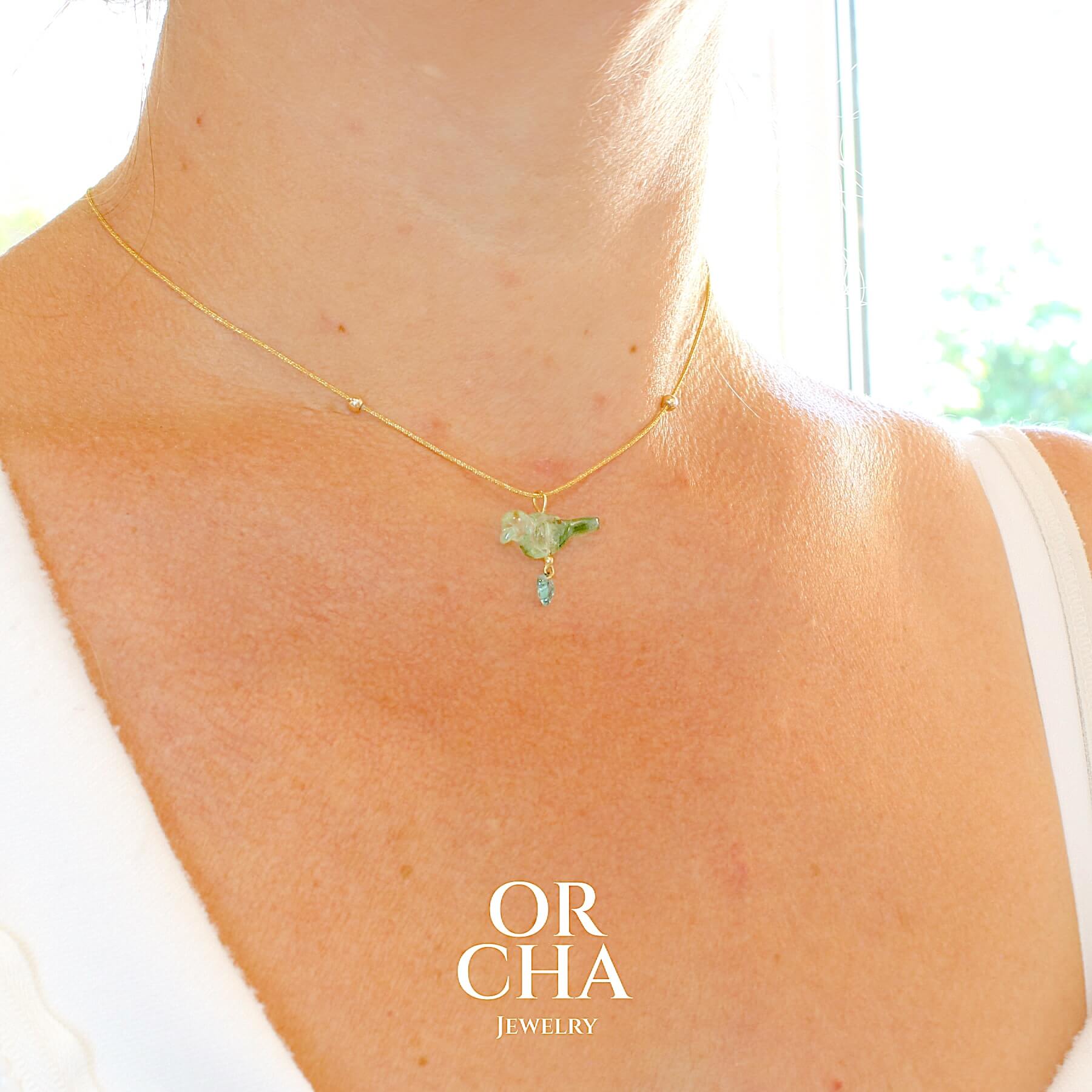 Collier Tourmaline verte bicolore sculptée à la main en 3 dimensions en forme d'oiseau plus une petite feuille, sertie en or 18k. Le pendentif est monté sur un collier corde doré scintillant, les apprêts utilisé sont en Gold filled ( or laminé ) Bijoux unique, éthique et durable présenté dans un coffret de notre marque, prêt à offrir. Livraison offerte, certificat d'authenticité, service client.