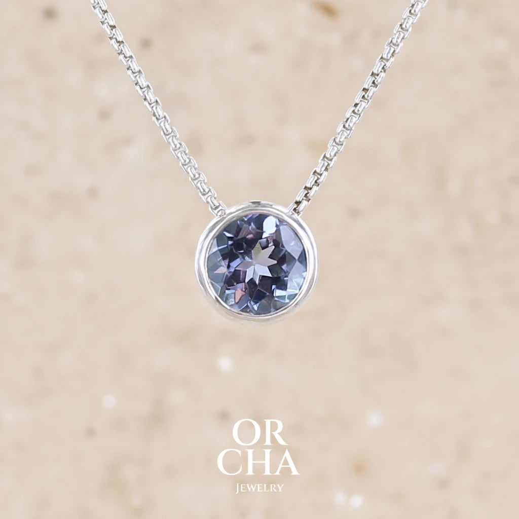 Collier solitaire pour femme en argent massif sertie d'une Tanzanite. Pierre facettée de forme ronde de qualité transparente, propre à l'oeil. Pierre naturelle de couleur bleu lavande avec de légers reflets verts. Pendentif monté sur une chaine en argent sterling de type maille vénitienne de 1,3 mm d'épaisseur et de 45 cm de longueur. Bijoux unique, éthique et durable présenté dans un coffret de notre marque, prêt à offrir. Livraison offerte, certificat d'authenticité, service client.