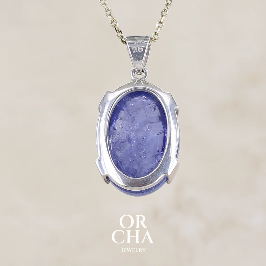 Vue de dos d'un pendentif en or 9k et argent massif serti d'un cabochon de Tanzanite de 46,3 carats, de couleur bleu lavande foncé profond et intense. Pierre transparente présentant des inclusions. Pierre ayant subit un traitement de chauffe, traitement admis et fréquent en gemmologie pour ce type de pierre . Bijoux unique, éthique et durable présenté dans un coffret de notre marque, prêt à offrir. Livraison offerte, certificat d'authenticité, service client.
