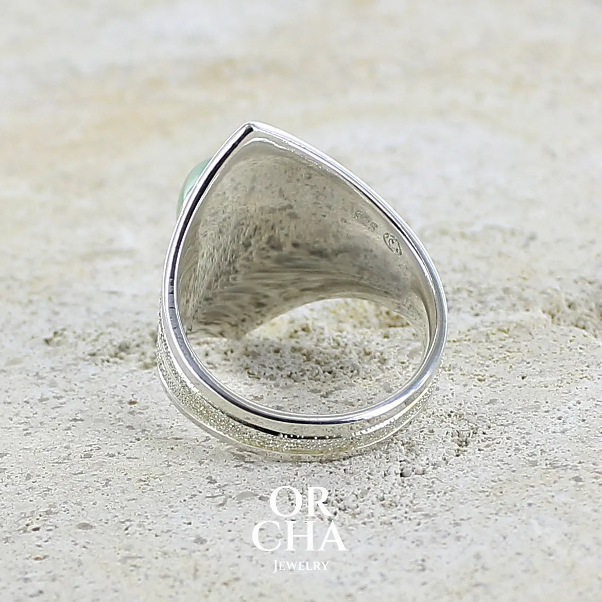 Vue de dos d'une bague pour femme en argent massif sculptées d'étoiles et autres corps célestes sertie d'un cabochon ovale de préhnite de couleur verte pastel lumineuse. Pierre naturelle de qualité transparente présentant des inclusions. Bijoux unique réalisé en taille 57 par Orchajewelry.