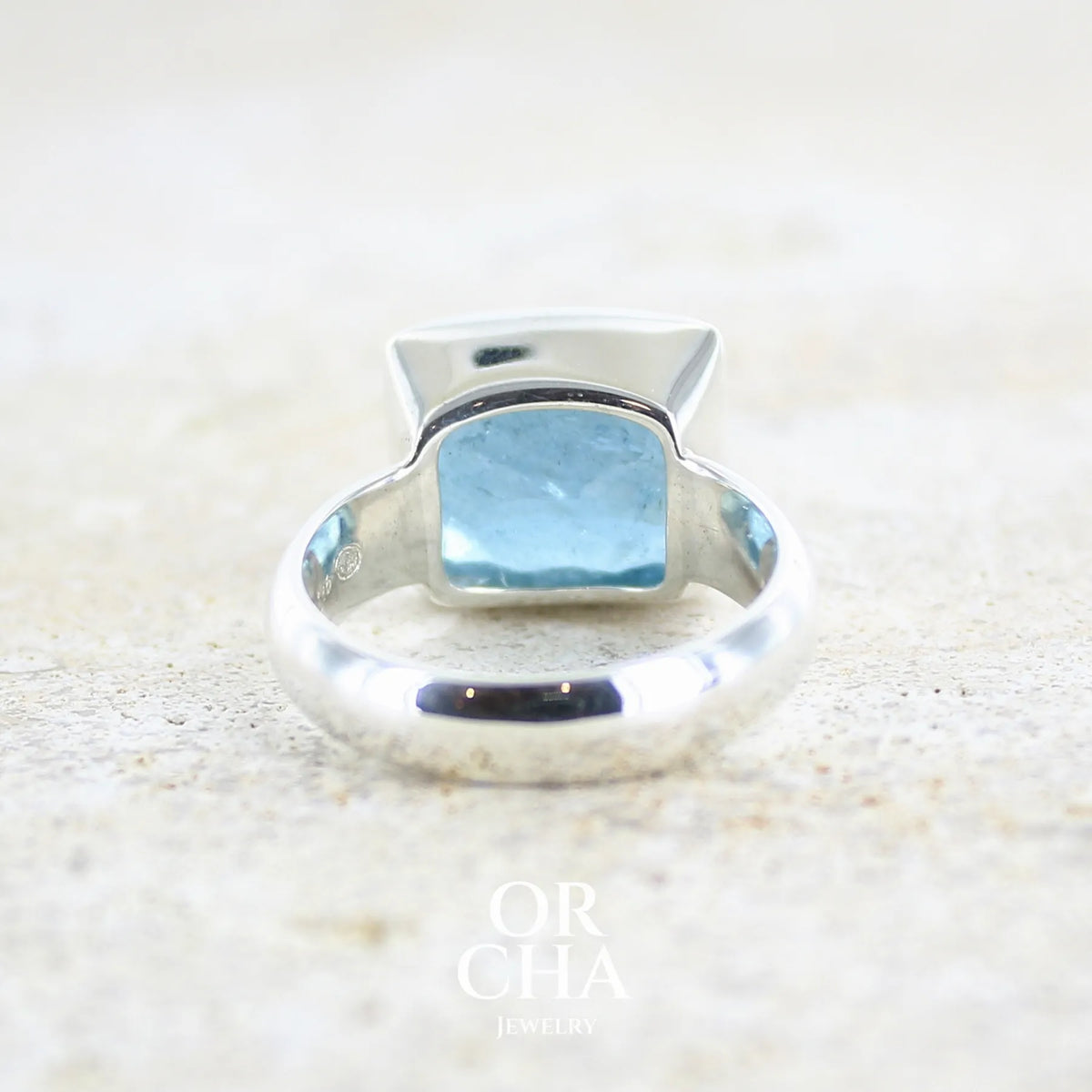 Vue de dos d'une Bague cocktail pour femme en argent massif sertie d'une aigue marine taillée de 10 carats de couleur bleue gris foncé, pierre transparente avec inclusions. Pierre naturelle facettée de forme rectangulaire. Bijoux unique réalisée en taille 60,5 par Orchajewelry