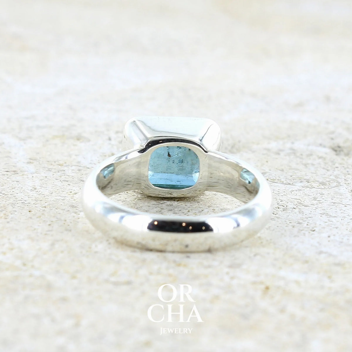 Vue de dos d'une bague pour femme en argent massif sertie d'une aigue marine taillée de 4 carats de couleur bleue foncé profonde  intense et lumineuse, pierre transparente avec inclusions. Pierre naturelle facettée de forme rectangulaire. Bijoux unique réalisée en taille 56 par Orchajewelry 
