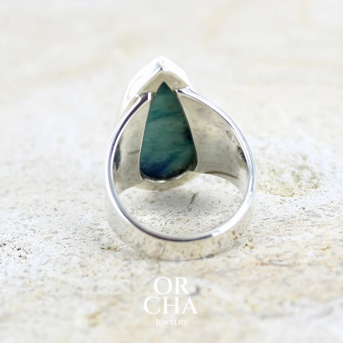 Vue de dos d'une bague pour femme en argent massif sertie d'un cabochon d'afghane de couleur bleu et bleu gris vert. Pierre taillée en forme de goutte de qualité opaque à inclusions (petites fissures) en surface, fréquente et admise sur ce type de pierre. Bijou unique réalisée en taille 58 par Orchajewelry