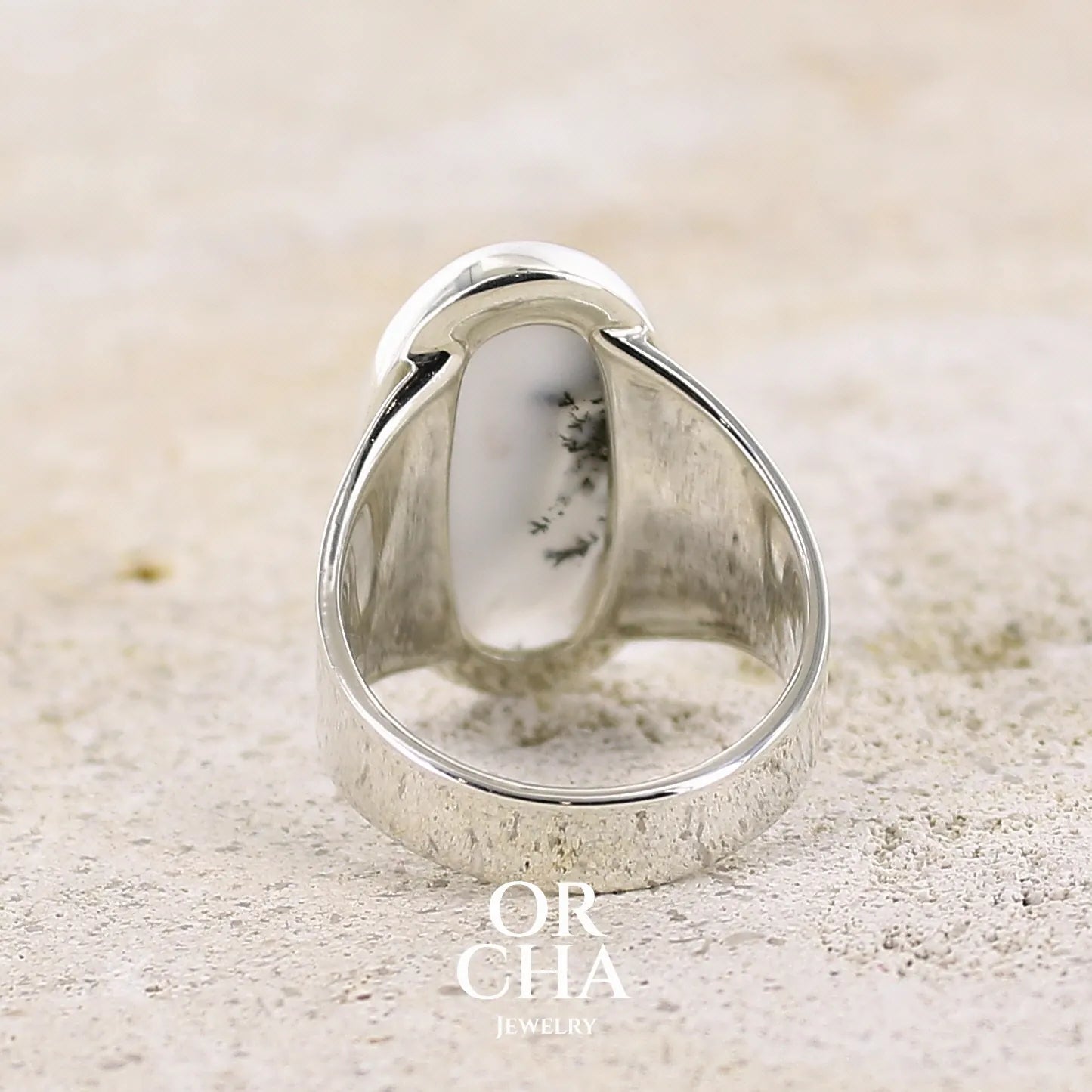 Vue de dos d'une bague pour femme en argent massif sertie d'un cabochon d'agate dendritique de couleur blanche et noire. Pierre de forme ovale de qualité translucide à inclusions paysages de manganèse contrastées. Bijou unique réalisée en taille 58 par Orcha Jewelry