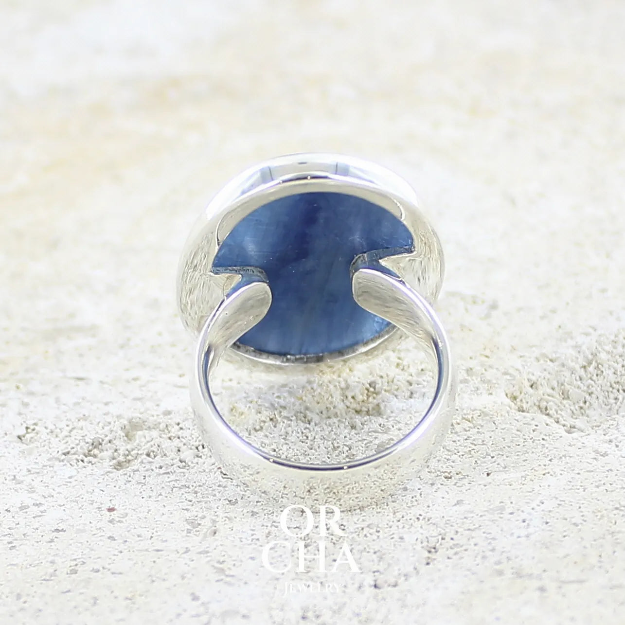 Vue de dos d'une bague pour femme en argent massif sertie d'un cabochon de cyanite de couleur bleu jean irisée. Pierre translucide à inclusions. Bijou unique réalisée en taille 56 par Orcha Jewelry