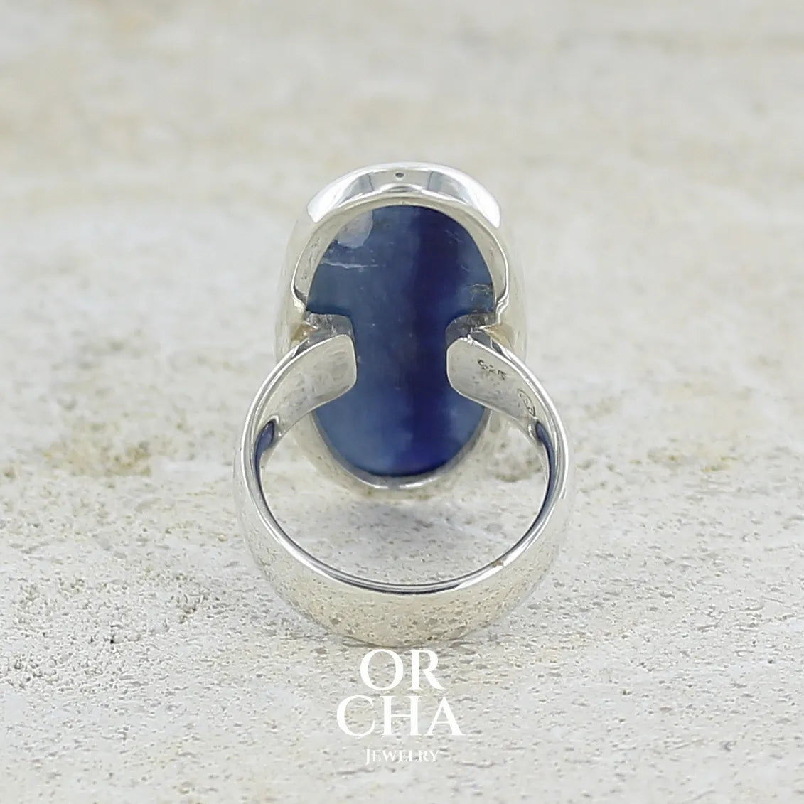 Vue de dos d'une bague pour femme en argent massif sertie d'un long cabochon ovale de cyanite bicolore de couleur bleu jean nacré. Pierre translucide à inclusions. Bijou unique réalisée en taille 54 par Orchajewelry