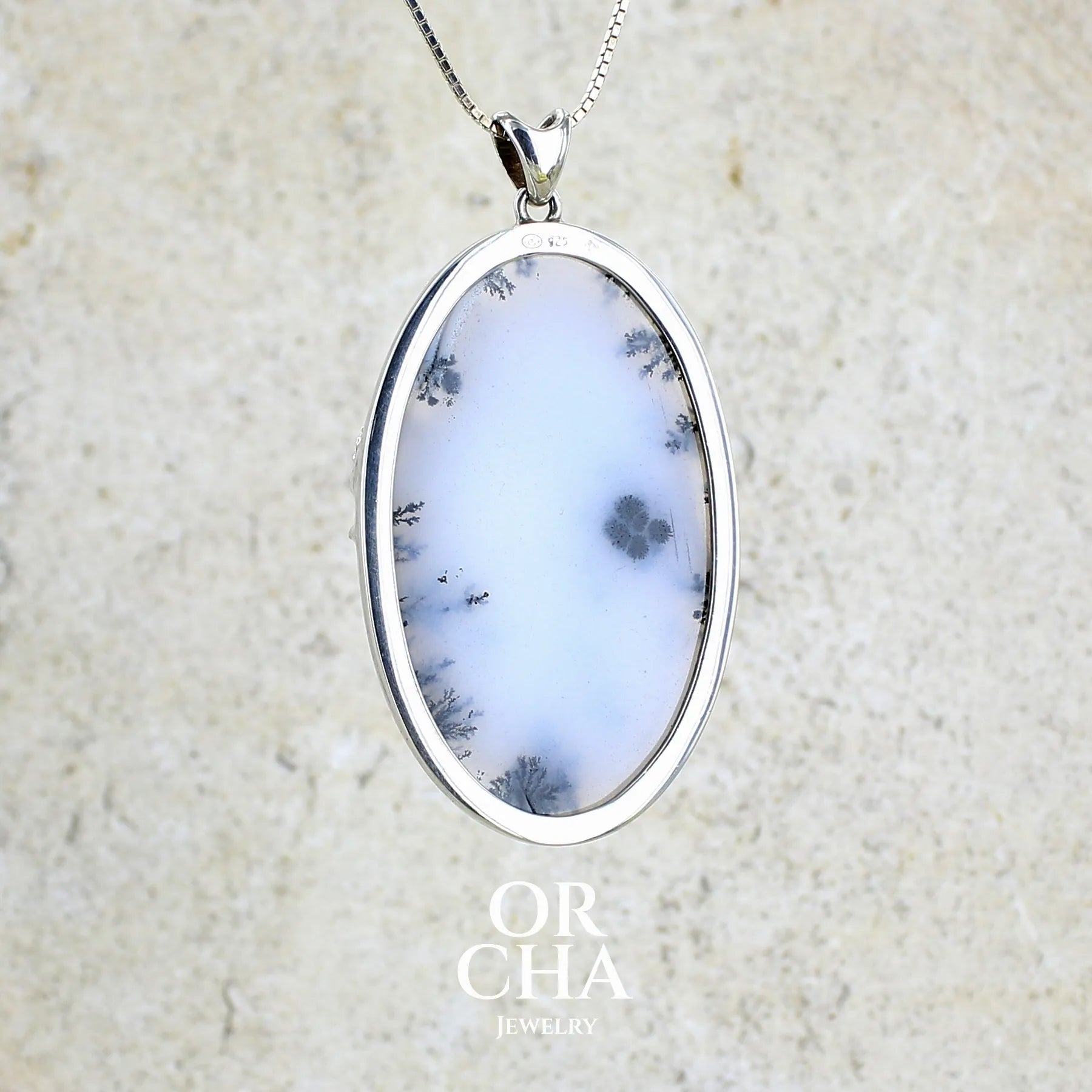 Vue de dos d'un pendentif en argent massif sertie d'un grand cabochon de forme ovale d'agate dendritique de couleur blanc pur et noir. Pierre opaque à translucide à inclusions paysages de dendrites de manganèse noires contrastées. Bijou unique illustré d'un cheval ailé réalisé par Orchajewelry