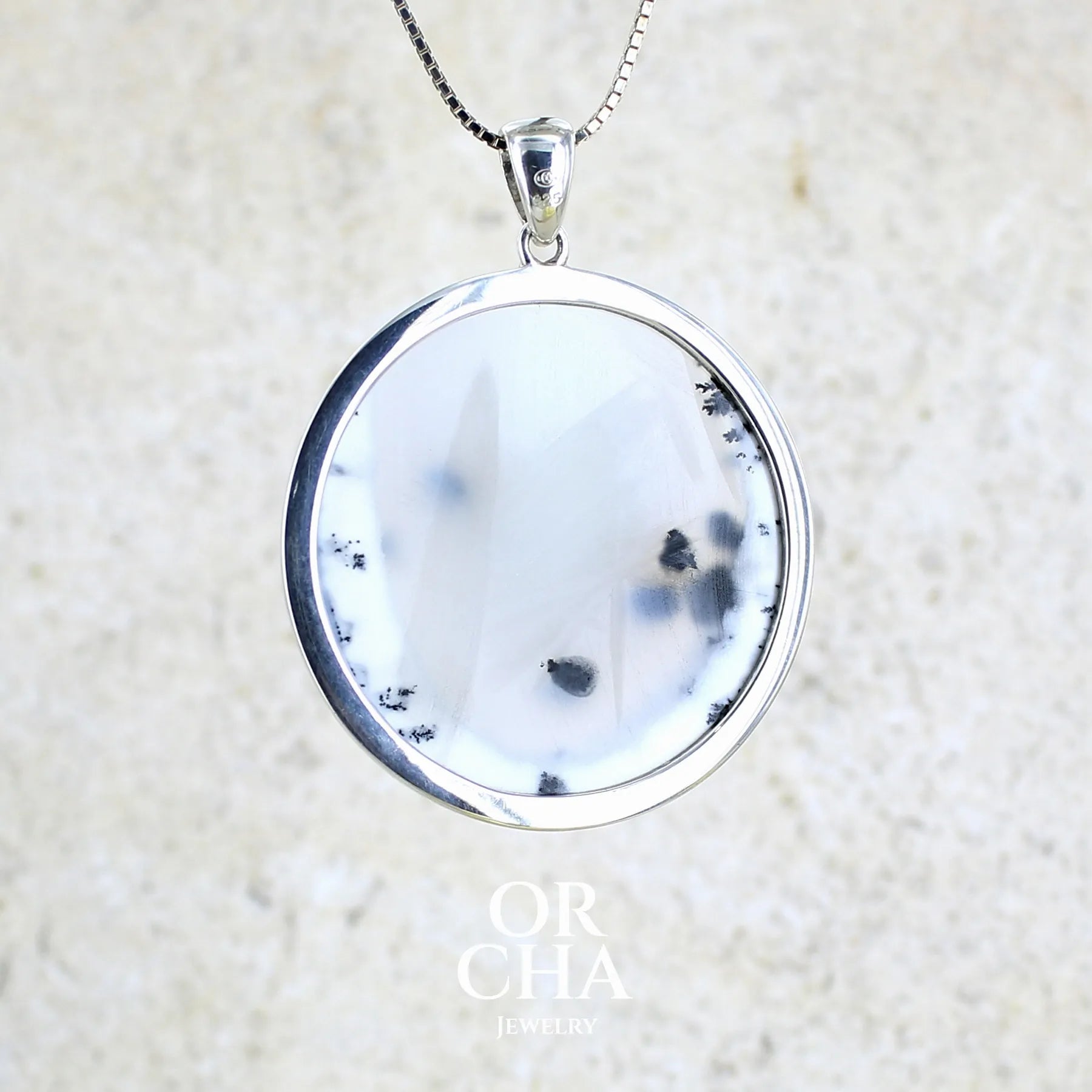 Vue de dos d'un pendentif pour femme en argent massif sertie d'un cabochon rond d'agate dendritique de couleur blanc pur et noir. Pierre opaque à translucide à inclusions paysages de dendrites de manganèse noires contrastées. Bijou unique réalisé par Orchajewelry