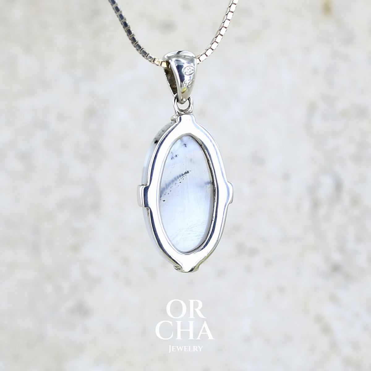 Vue de dos d'un pendentif pour femme en argent massif sertie d'un cabochon de forme ovale d'agate dendritique de couleur blanc pur et noir. Pierre opaque à translucide à inclusions paysages de dendrites de manganèse noires contrastées. Bijou unique réalisé par Orchajewelry