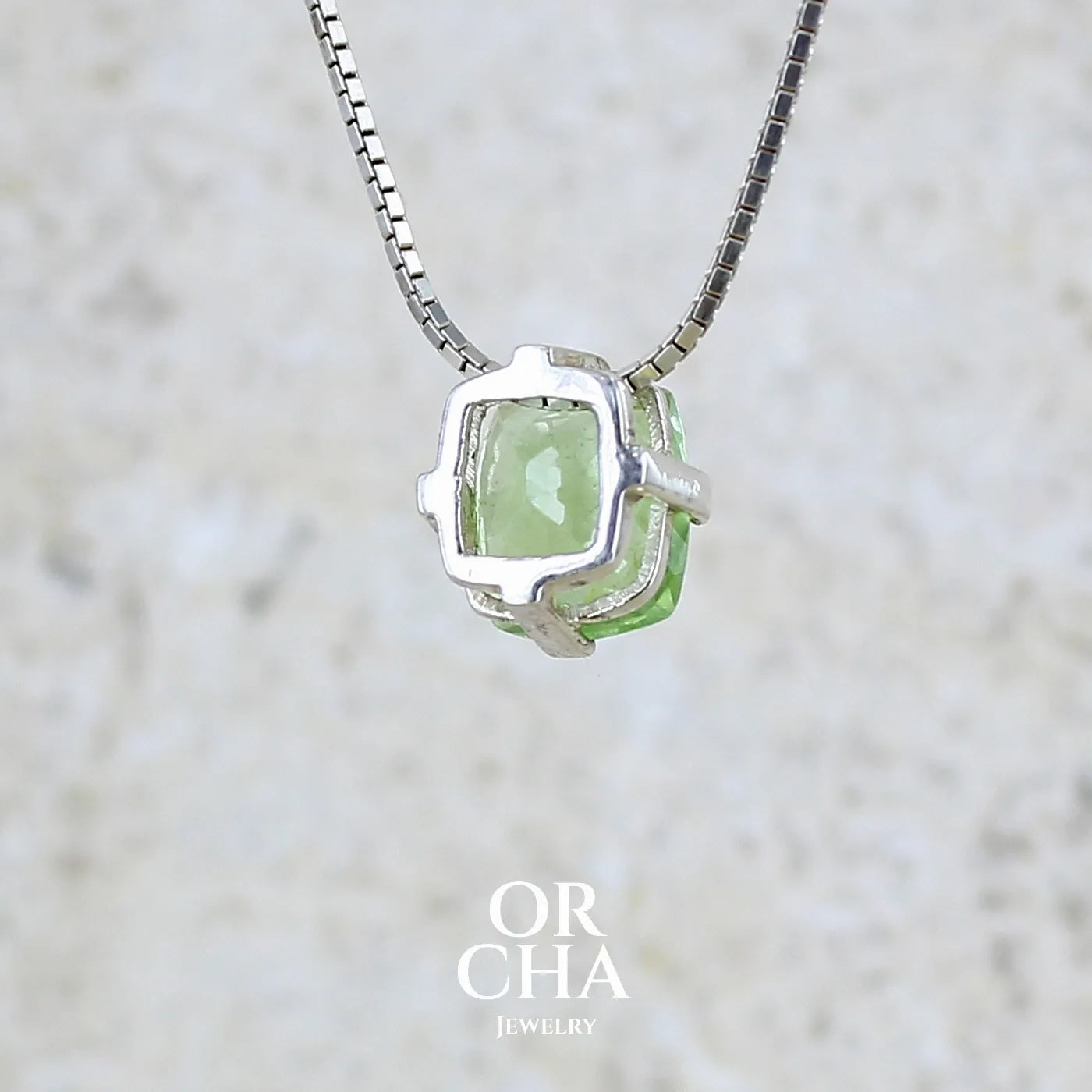 Vue de dos d'un collier solitaire pour femme en argent massif sertie d'un Péridot de couleur vert pastel anisé. Pierre facettée de forme carrée, qualité transparente présentant des inclusions. Pendentif monté sur une chaine en argent sterling de type maille miroir de 1,3 mm d'épaisseur et de 40cm de longueur. Bijoux unique réalisé par Orchajewelry