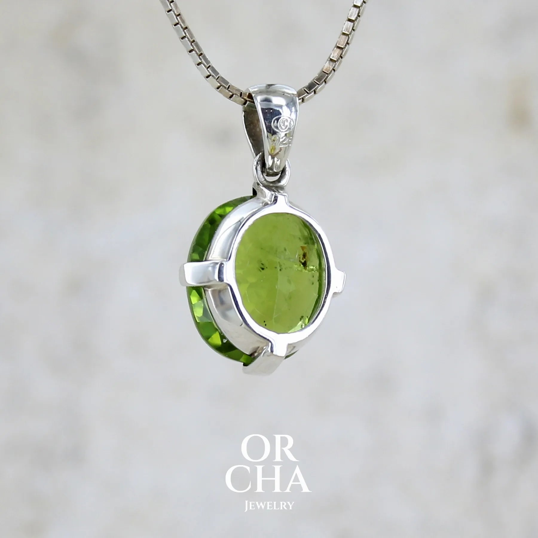 Vue de dos d'un pendentif pour femme en argent massif serti d'un péridot de couleur vert olive doré intense. Pierre taillée, de forme ovale, transparente présentant de nombreuse inclusions. Bijou unique réalisé par Orchajewelry