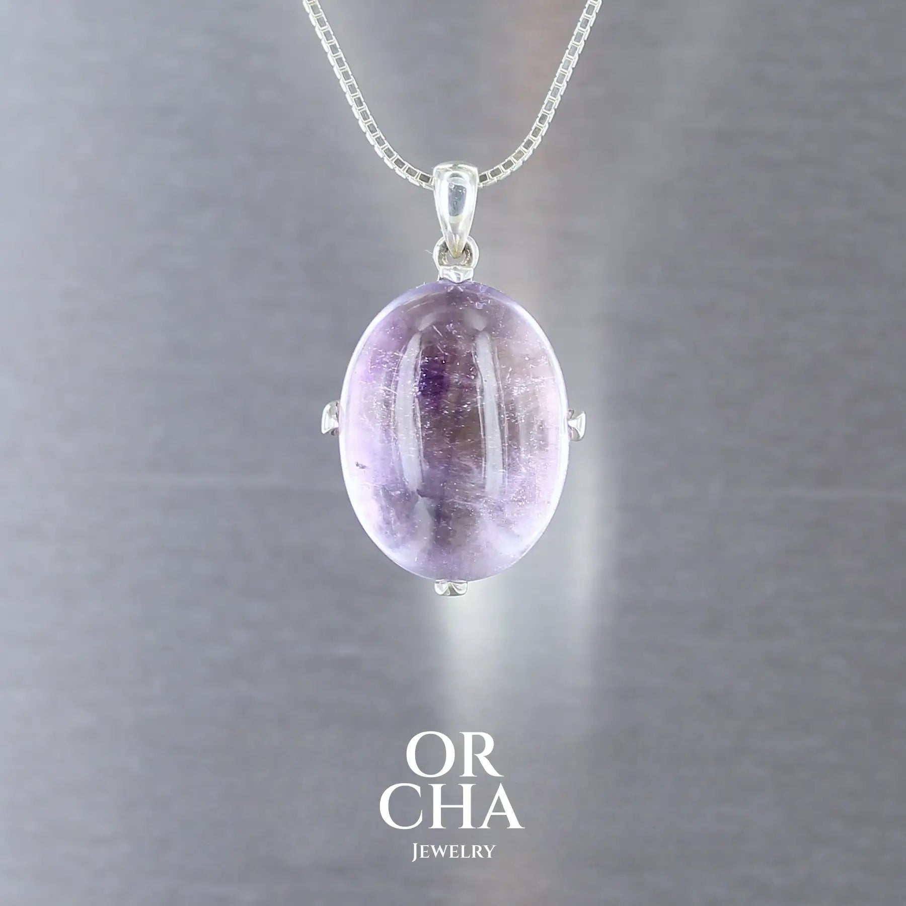 pendentif pour femme en argent massif serti d'un cabochon Améthyste de 37,7 carats de couleur violette clair à incolore et nuage violet foncé. Pierre naturelle transparente présentant des inclusions. Bijoux unique, éthique et durable présenté dans un coffret de notre marque, prêt à offrir. Livraison offerte, certificat d'authenticité, service client.
