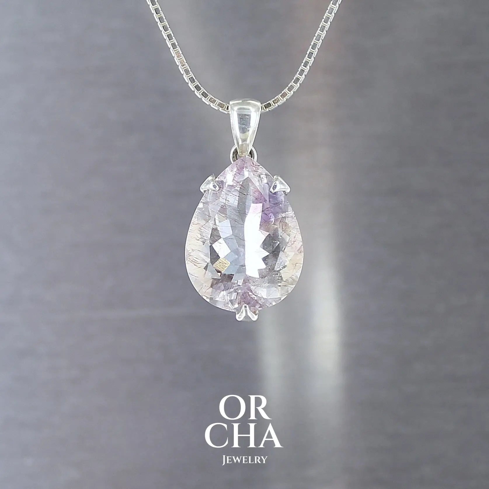 pendentif pour femme en argent massif serti d'une Améthyste de 12 carats de couleur blanc transparent, violet très clair et inclusions d'hématite rouge. Pierre facettée naturelle transparente présentant des inclusions. Bijoux unique, éthique et durable présenté dans un coffret de notre marque, prêt à offrir. Livraison offerte, certificat d'authenticité, service client.
