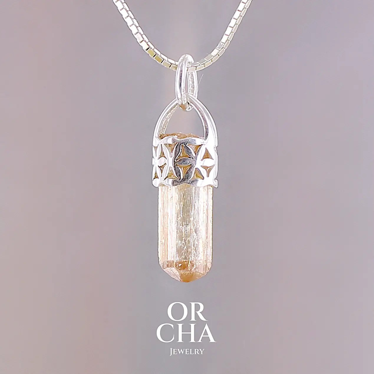 Pendentif cristal de topaze impériale en argent massif, sertissage filigrané de fleurs de vie. La pierre est  de couleur jaune arrangé pêche. Cristal brute, transparent, inclusions naturelles. Bijoux unique, éthique et durable présenté dans un coffret de notre marque, prêt à offrir. Livraison offerte, certificat d'authenticité, service client.