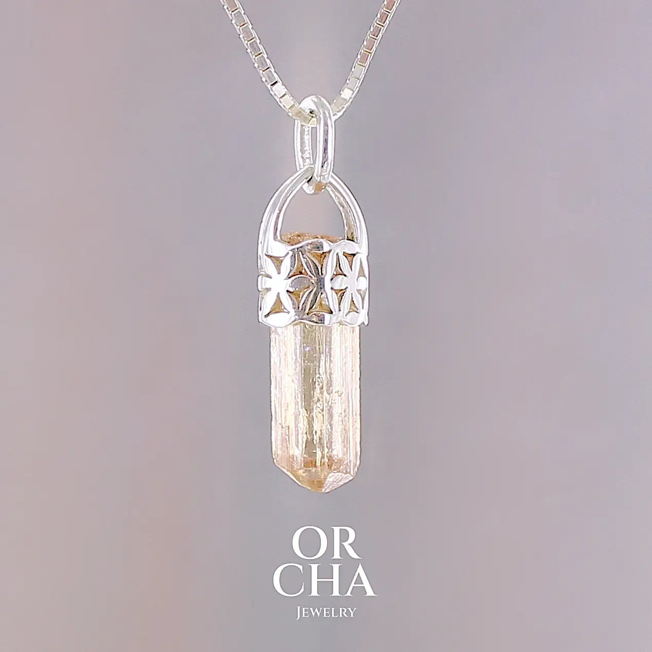Pendentif cristal de topaze impériale en argent massif, sertissage filigrané de fleurs de vie. La pierre est  de couleur jaune arrangé pêche. Cristal brute, transparent, inclusions naturelles. Bijoux unique, éthique et durable présenté dans un coffret de notre marque, prêt à offrir. Livraison offerte, certificat d'authenticité, service client.