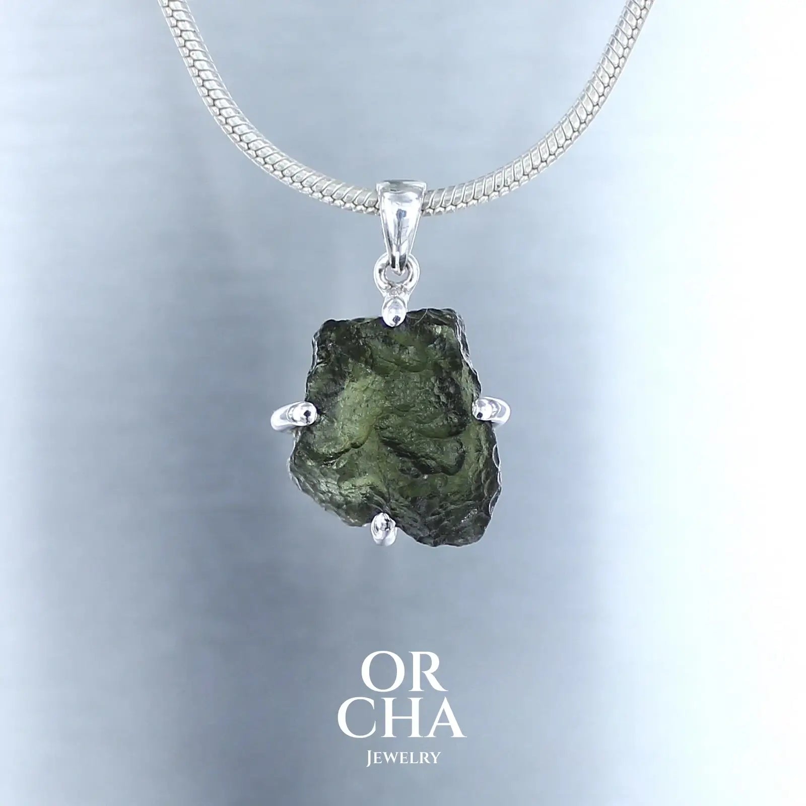 pendentif pour homme en argent massif serti d'une Moldavite brute de couleur verte foncée. Pierre naturelle brute transparente. Bijoux unique, éthique et durable présenté dans un coffret de notre marque, prêt à offrir. Livraison offerte, certificat d'authenticité, service client.