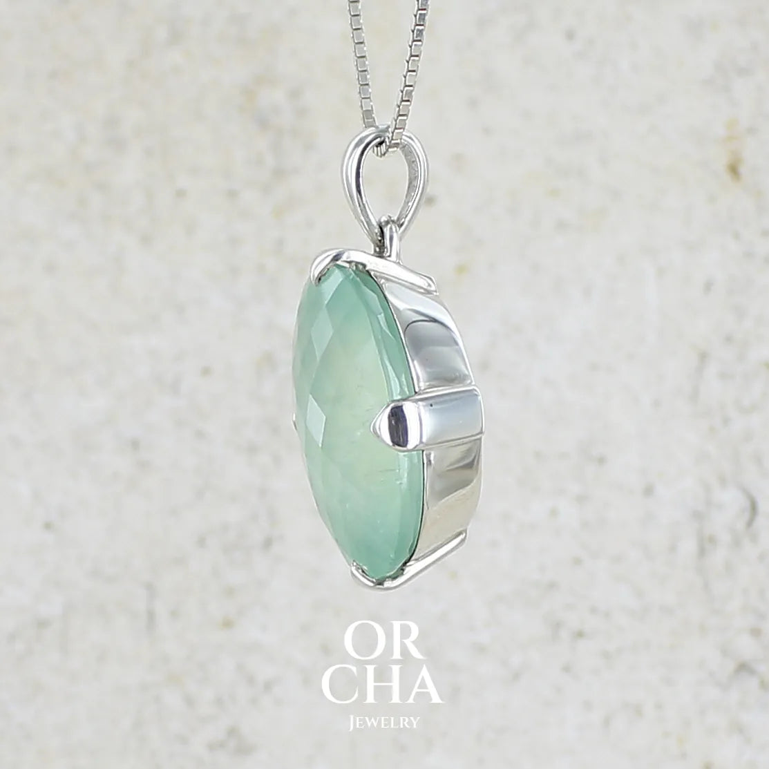 Détail du sertissage d'un pendentif ovale en argent massif, serti d'un cabochon facetté de préhnite de couleur verte pastel. Pierre de qualité translucide comportant des inclusions. Bijoux unique par Orcha Jewelry