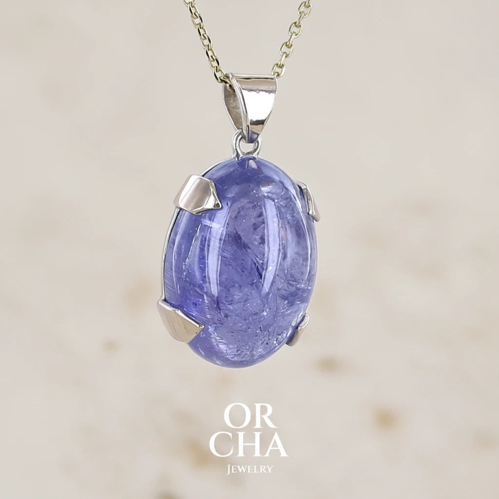 Profil droit d'un pendentif en or 9k et argent massif serti d'un cabochon de Tanzanite de 46,3 carats, de couleur bleu lavande foncé profond et intense. Pierre transparente présentant des inclusions. Pierre ayant subit un traitement de chauffe, traitement admis et fréquent en gemmologie pour ce type de pierre . Bijoux unique, éthique et durable présenté dans un coffret de notre marque, prêt à offrir. Livraison offerte, certificat d'authenticité, service client.