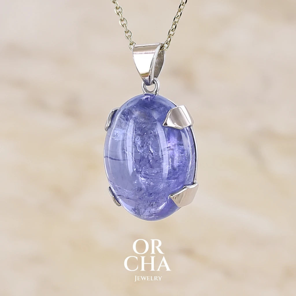 Profil gauche d'un pendentif en or 9k et argent massif serti d'un cabochon de Tanzanite de 46,3 carats, de couleur bleu lavande foncé profond et intense. Pierre transparente présentant des inclusions. Pierre ayant subit un traitement de chauffe, traitement admis et fréquent en gemmologie pour ce type de pierre . Bijoux unique, éthique et durable présenté dans un coffret de notre marque, prêt à offrir. Livraison offerte, certificat d'authenticité, service client.