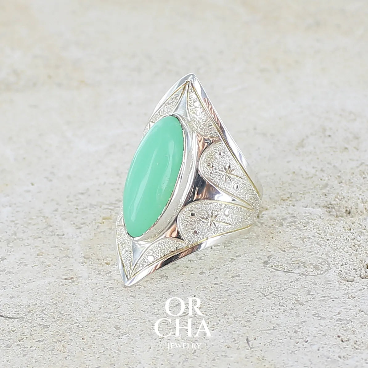 Profil gauche d'une bague marquise pour femme en argent massif sculptées d'étoiles et autres corps célestes sertie d'un cabochon de chrysoprase de couleur verte pastel. Pierre naturelle de qualité translucide taillée en ovale longiligne. Bague unique réalisée en taille 57 par Orcha jewelry