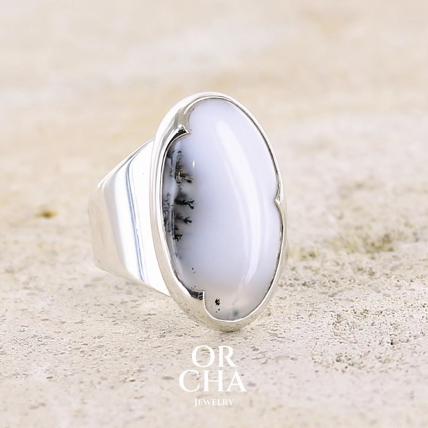 Profil droit d'une bague pour femme en argent massif sertie d'un cabochon d'agate dendritique de couleur blanche et noire. Pierre de forme ovale de qualité translucide à inclusions paysages de manganèse contrastées. Bijou unique réalisée en taille 58 par Orcha Jewelry