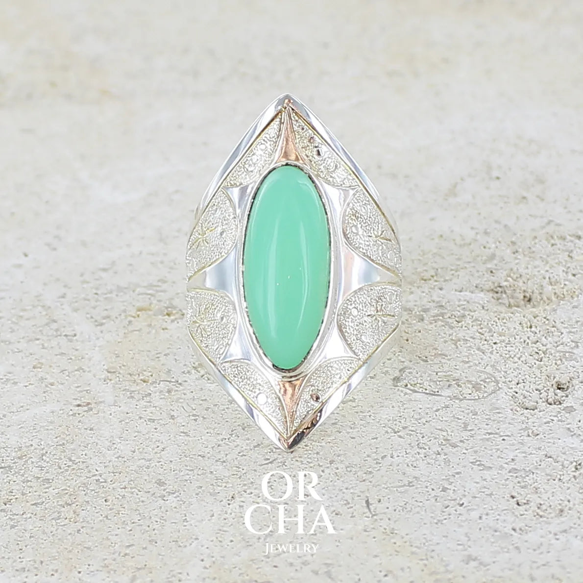 Bague marquise pour femme en argent massif sculptées d'étoiles et autres corps célestes sertie d'un cabochon de chrysoprase de couleur verte pastel. Pierre naturelle de qualité translucide taillée en ovale longiligne. Bague unique réalisée en taille 57 par Orcha jewelry