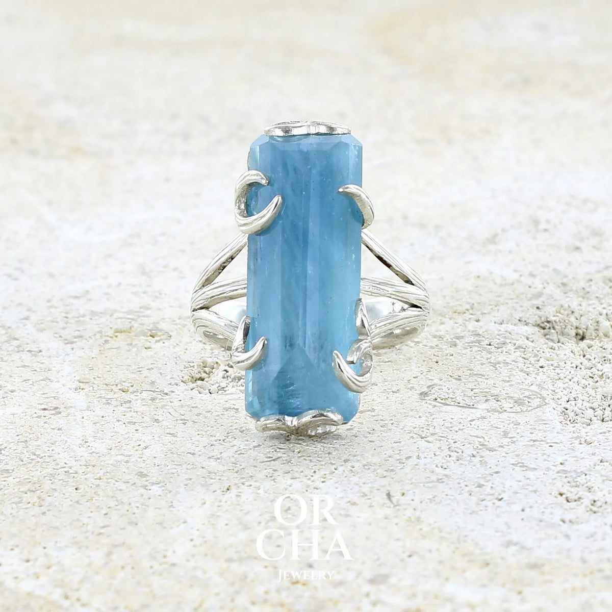 Bague cocktail pour femme en argent massif sertie d'une aigue marine taillée de 15 carats de couleur bleue gris trouble, pierre transparente avec inclusions. Pierre naturelle facettée de forme rectangulaire. Bijoux unique réalisée en taille 54,5 par Orchajewelry 