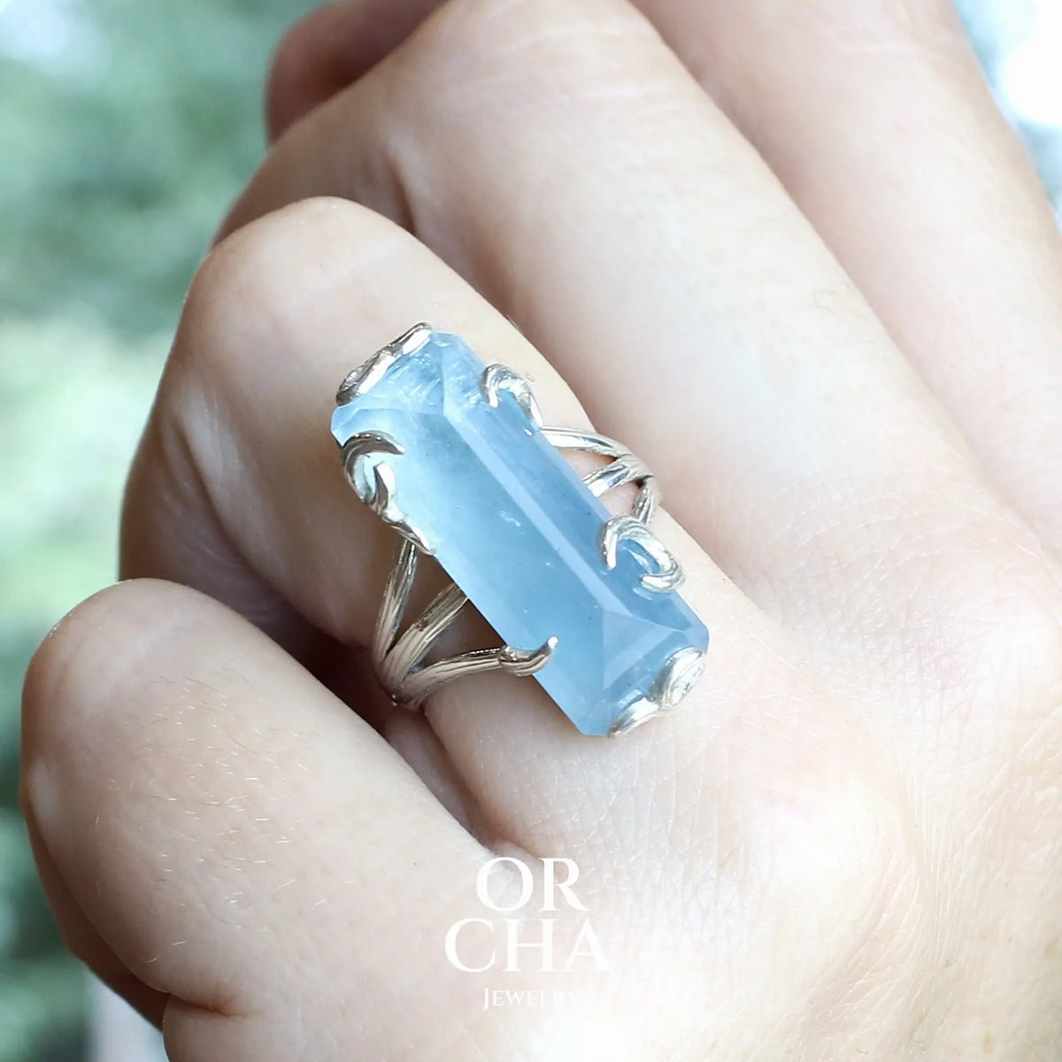 Bague cocktail pour femme en argent massif sertie d'une aigue marine taillée de 15 carats de couleur bleue gris trouble, pierre transparente avec inclusions. Pierre naturelle facettée de forme rectangulaire. Bijoux unique réalisée en taille 54,5 par Orchajewelry 