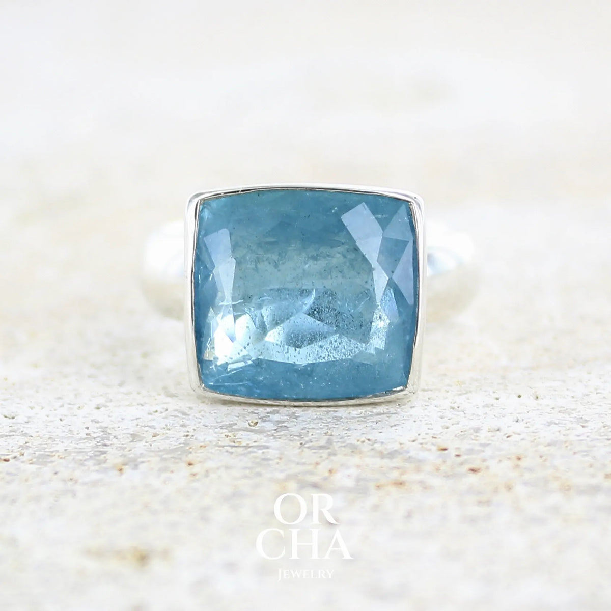 Bague cocktail pour femme en argent massif sertie d'une aigue marine taillée de 10 carats de couleur bleue gris foncé, pierre transparente avec inclusions. Pierre naturelle facettée de forme rectangulaire. Bijoux unique réalisée en taille 60,5 par Orchajewelry
