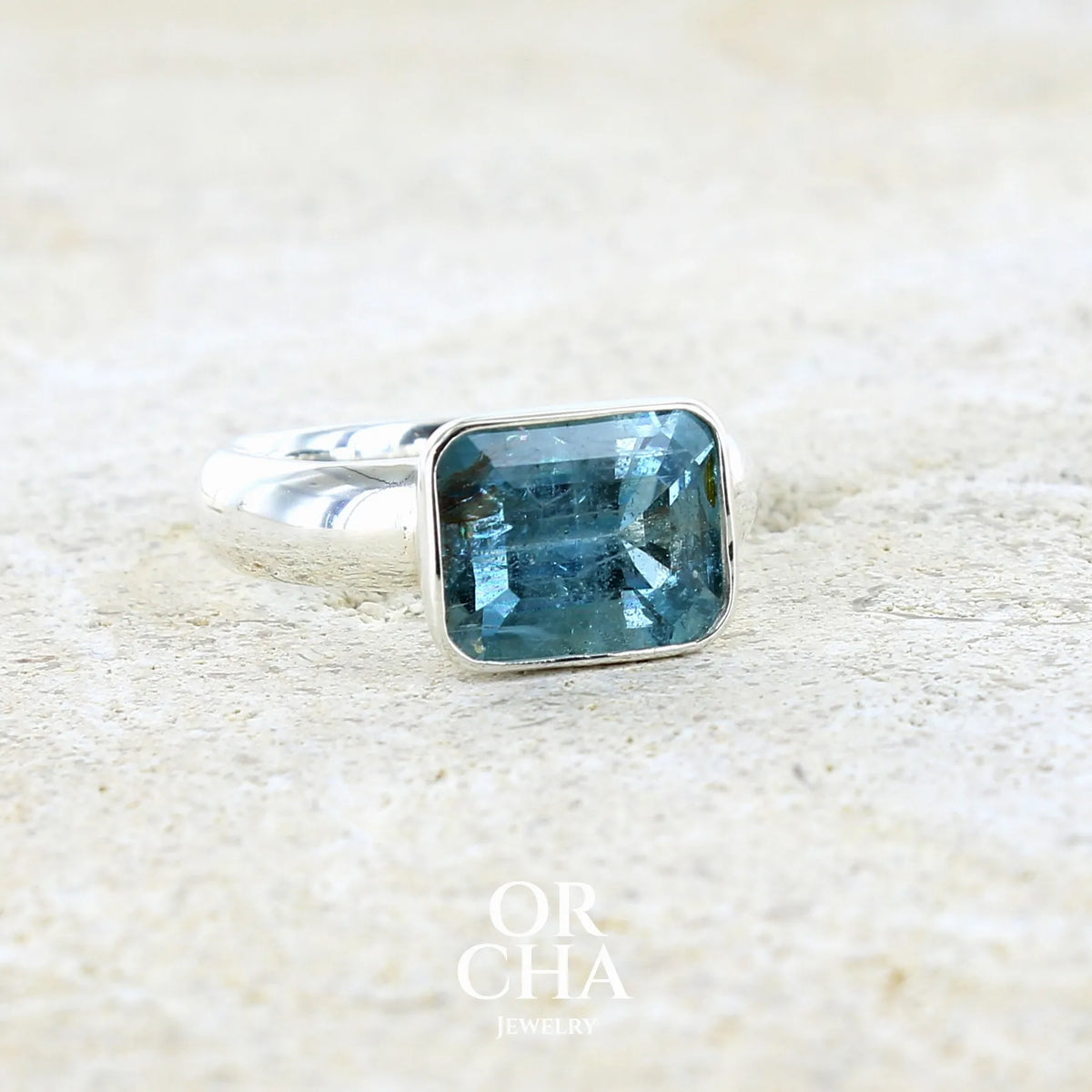 Bague pour femme en argent massif sertie d'une aigue marine taillée de 4 carats de couleur bleue foncé profonde  intense et lumineuse, pierre transparente avec inclusions. Pierre naturelle facettée de forme rectangulaire. Bijoux unique réalisée en taille 56 par Orchajewelry 