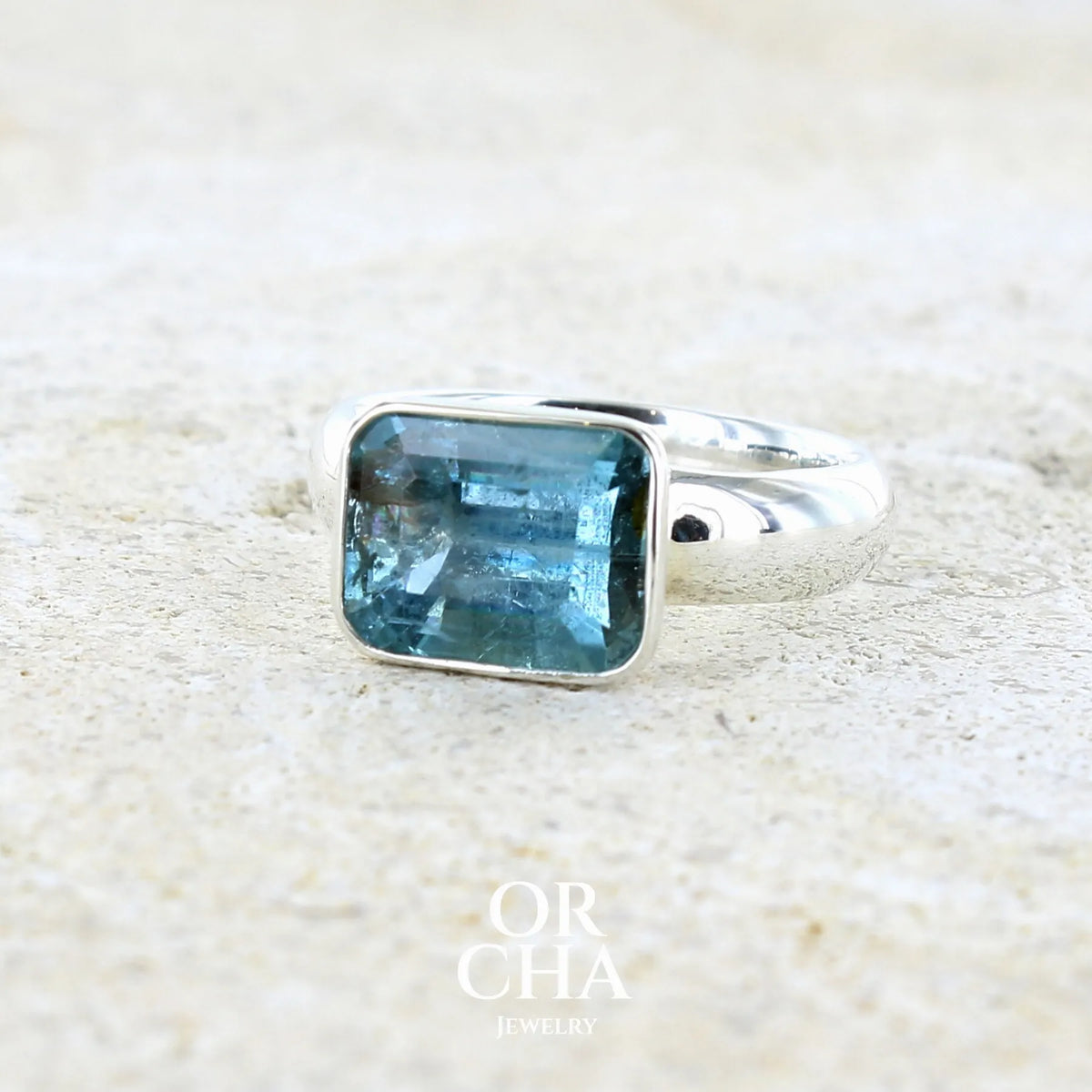 Bague pour femme en argent massif sertie d'une aigue marine taillée de 4 carats de couleur bleue foncé profonde  intense et lumineuse, pierre transparente avec inclusions. Pierre naturelle facettée de forme rectangulaire. Bijoux unique réalisée en taille 56 par Orchajewelry 