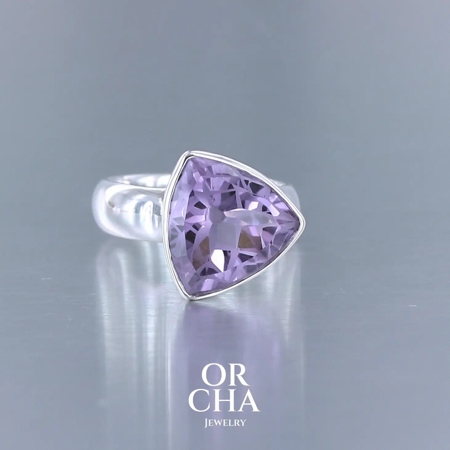 Bague cocktail pour femme en argent massif sertie d'une Améthyste. Pierre taillée trillion de qualité transparente, propre à l'oeil. Pierre naturelle de couleur violette clair gravée de motifs géométriques de fleur de vie. Tailles 58. Bijoux unique, éthique et durable présenté dans un coffret de notre marque, prêt à offrir. Livraison offerte, certificat d'authenticité, service client.