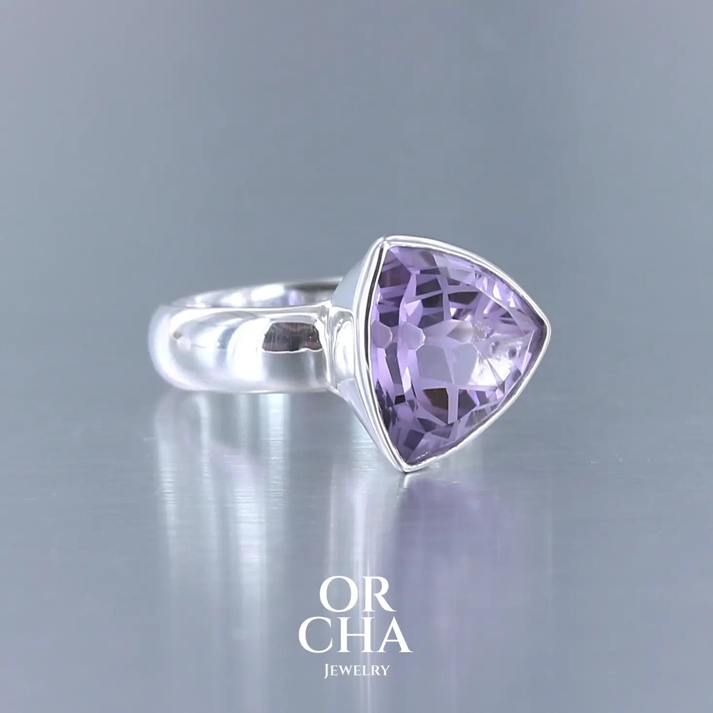 Bague cocktail pour femme en argent massif sertie d'une Améthyste. Pierre taillée trillion de qualité transparente, propre à l'oeil. Pierre naturelle de couleur violette clair gravée de motifs géométriques de fleur de vie. Tailles 58. Bijoux unique, éthique et durable présenté dans un coffret de notre marque, prêt à offrir. Livraison offerte, certificat d'authenticité, service client.