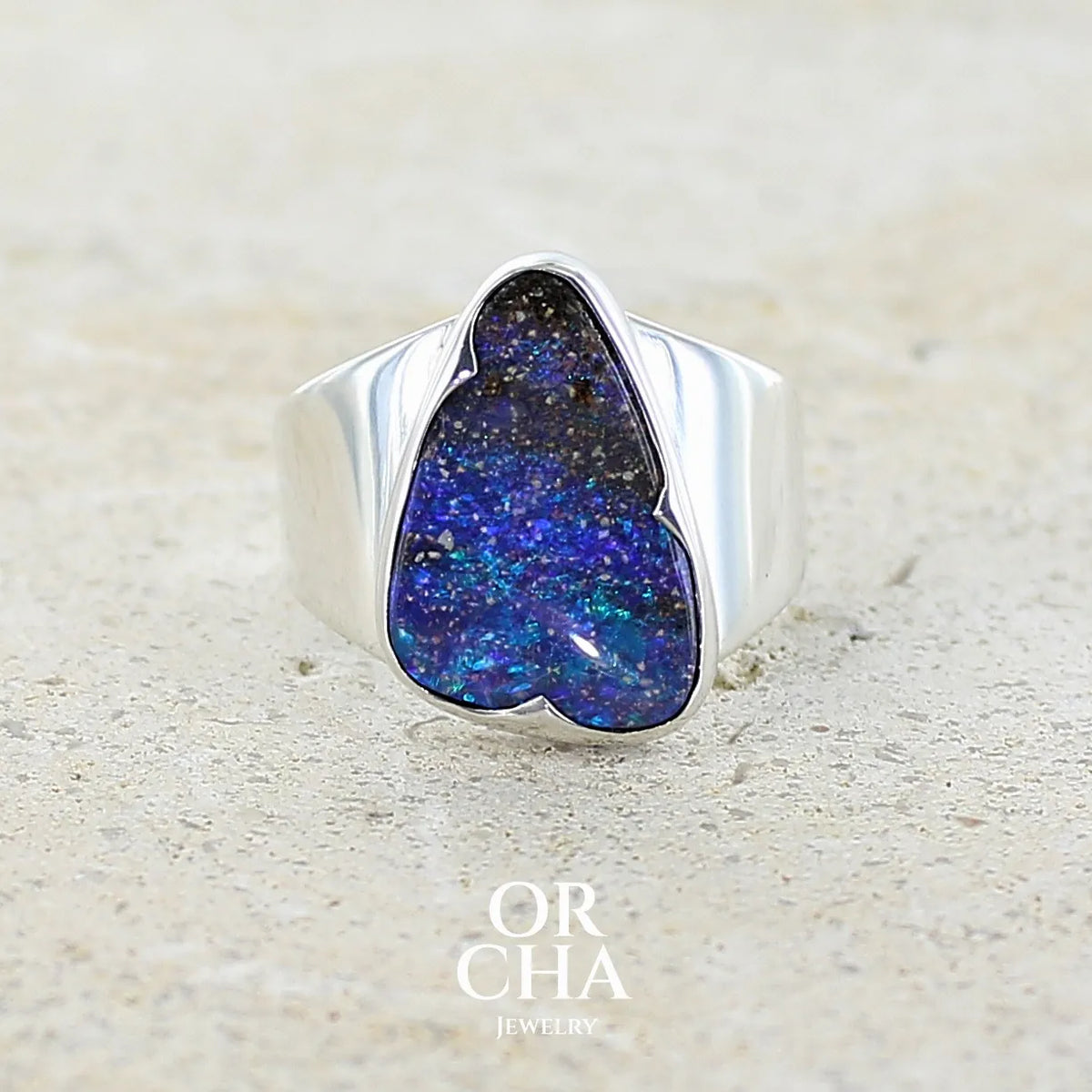 Bague pour femme en argent massif 925 sertie d'une opale boulder aux feux multicolores bleus violet et verts. Cabochon d'opale massive naturelle taillée en forme d'aile. Pierre de qualité opaque. Bijoux unique réalisé en taille 58 par Orcha Jewelry.