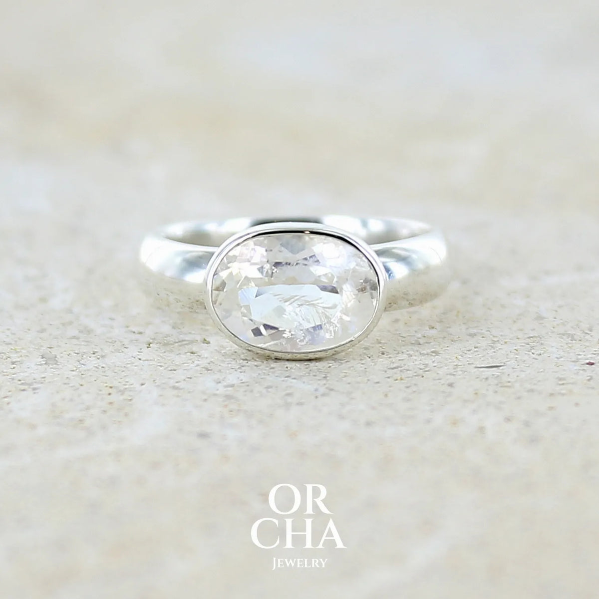 Bague cocktail pour femme en argent massif 925 sertie d'une pierre de lune de Madagascar taillée de 2,18 carats, pierre incolore aux reflets orangés et arc en ciel. Pierre transparente avec inclusions. Bijoux unique réalisé en taille 52 par Orcha Jewelry