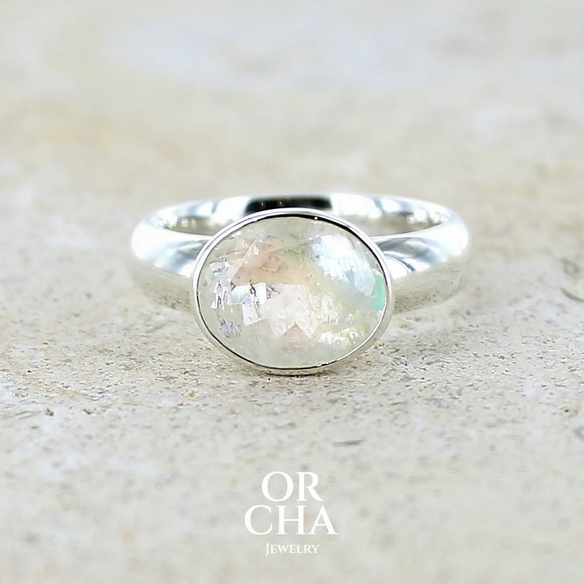 Bague cocktail pour femme en argent massif 925 sertie d'une pierre de lune arc en ciel de Madagascar taillée de 2,5 carats incolore aux reflets bleutés et arc en ciel. Pierre transparente avec inclusions. Bijoux unique réalisée en taille 56 par Orchajewelry