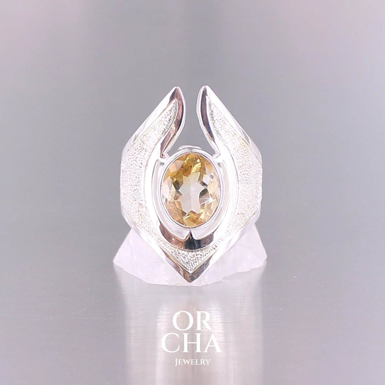 Grande bague contemporaine pour femme en argent massif sertie d'une Citrine. Pierre facettée de forme ovale de qualité transparente, propre à l'oeil. Pierre naturelle de couleur jaune doré lumineux. Bijoux unique, éthique et durable présenté dans un coffret de notre marque, prêt à offrir. Livraison offerte, certificat d'authenticité, service client.
